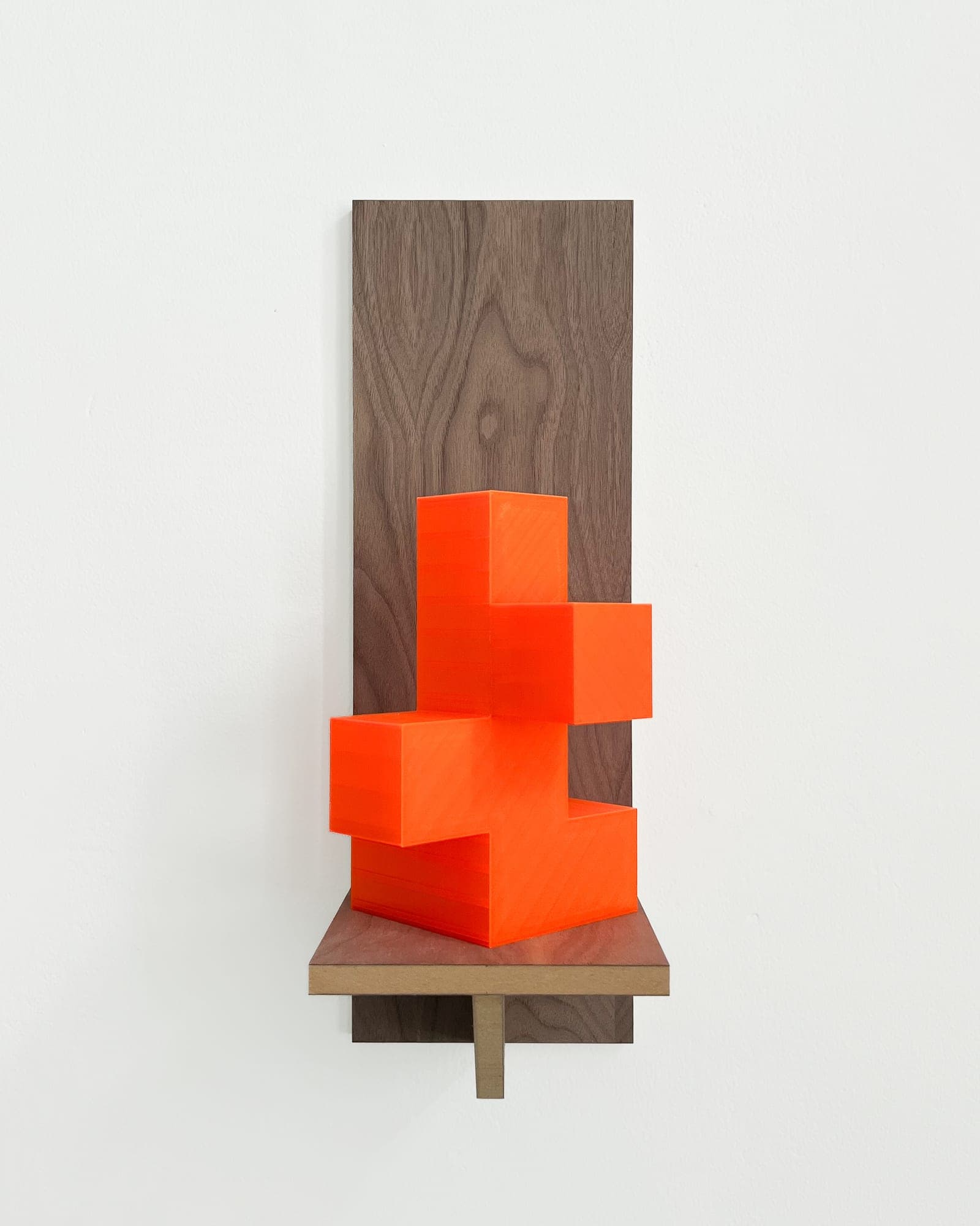 Wall-mounted walnut panel sculpture with a neon-orange 3D-printed stepped block form