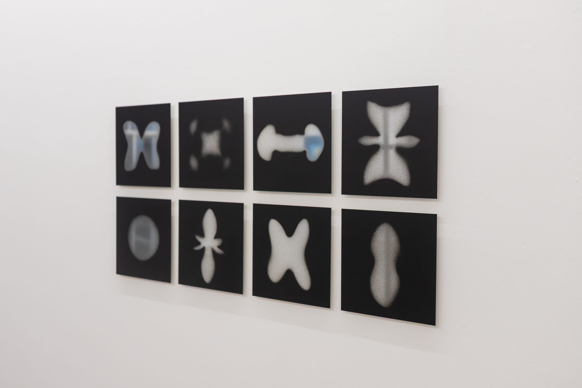 Grid of eight black square photographs of soft spray-painted atom-like shapes