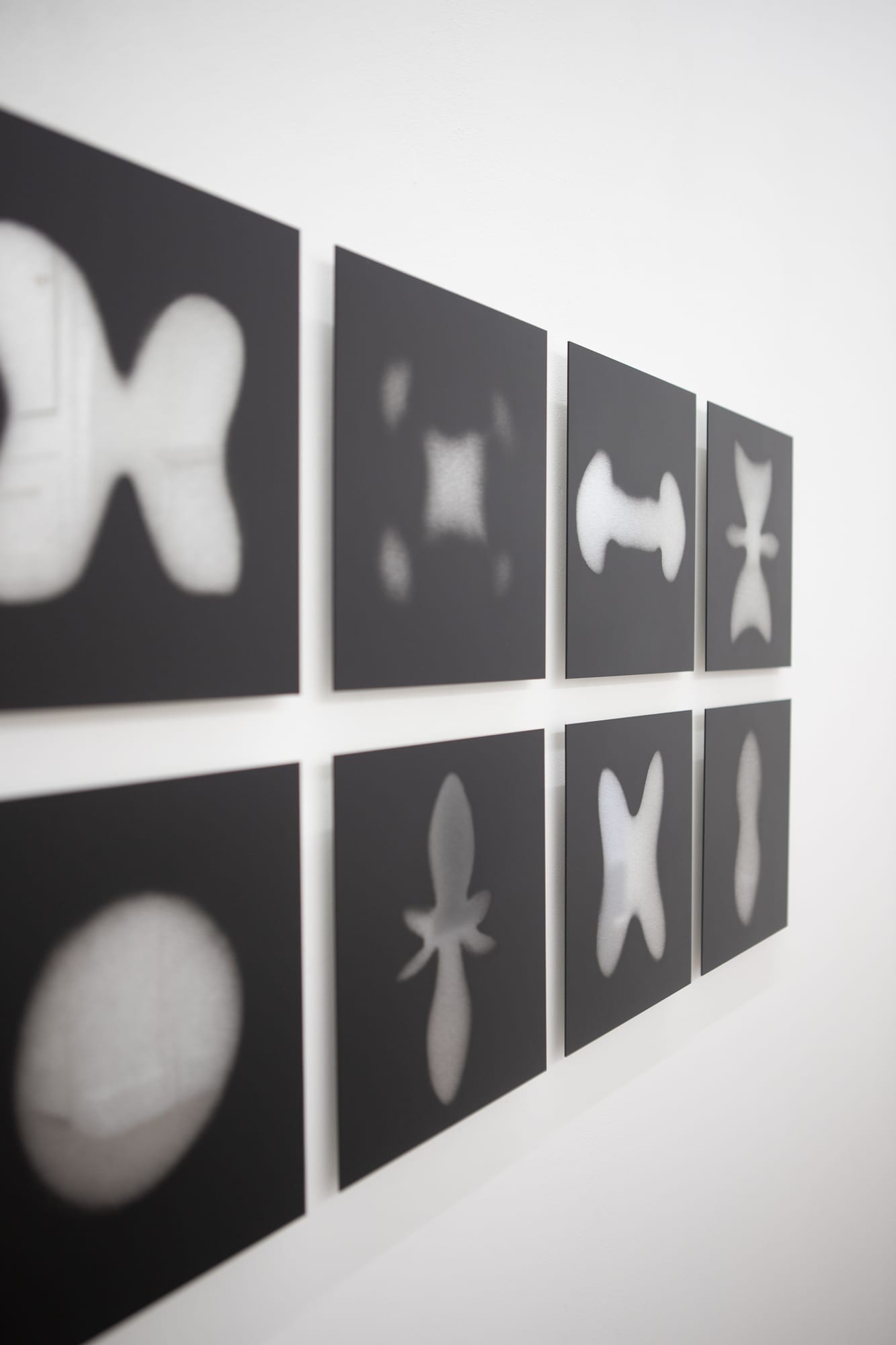 Angled installation view of the grid of eight atom-shape photographs