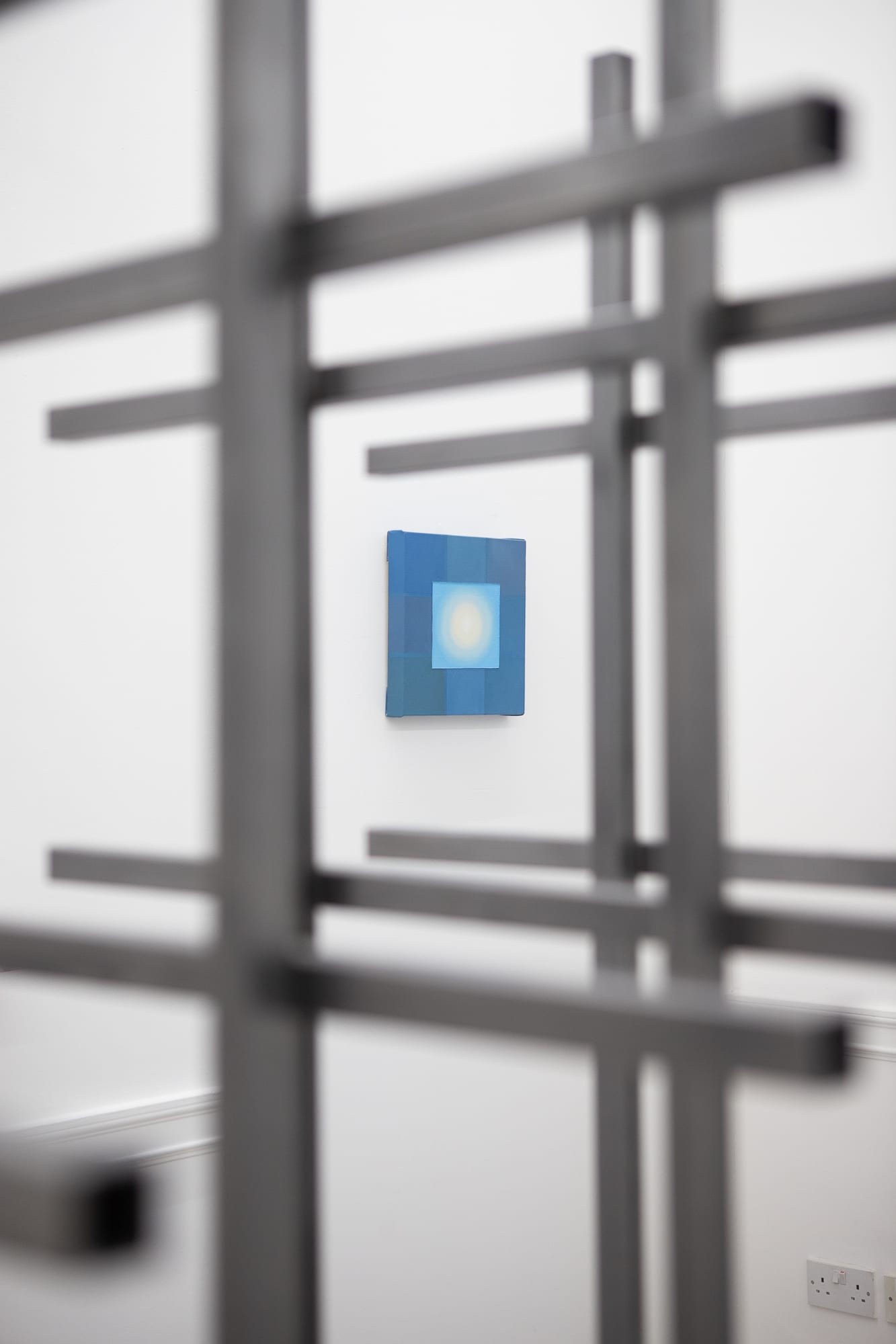Blurred steel grid sculpture in front of a small blue painting with a glowing center