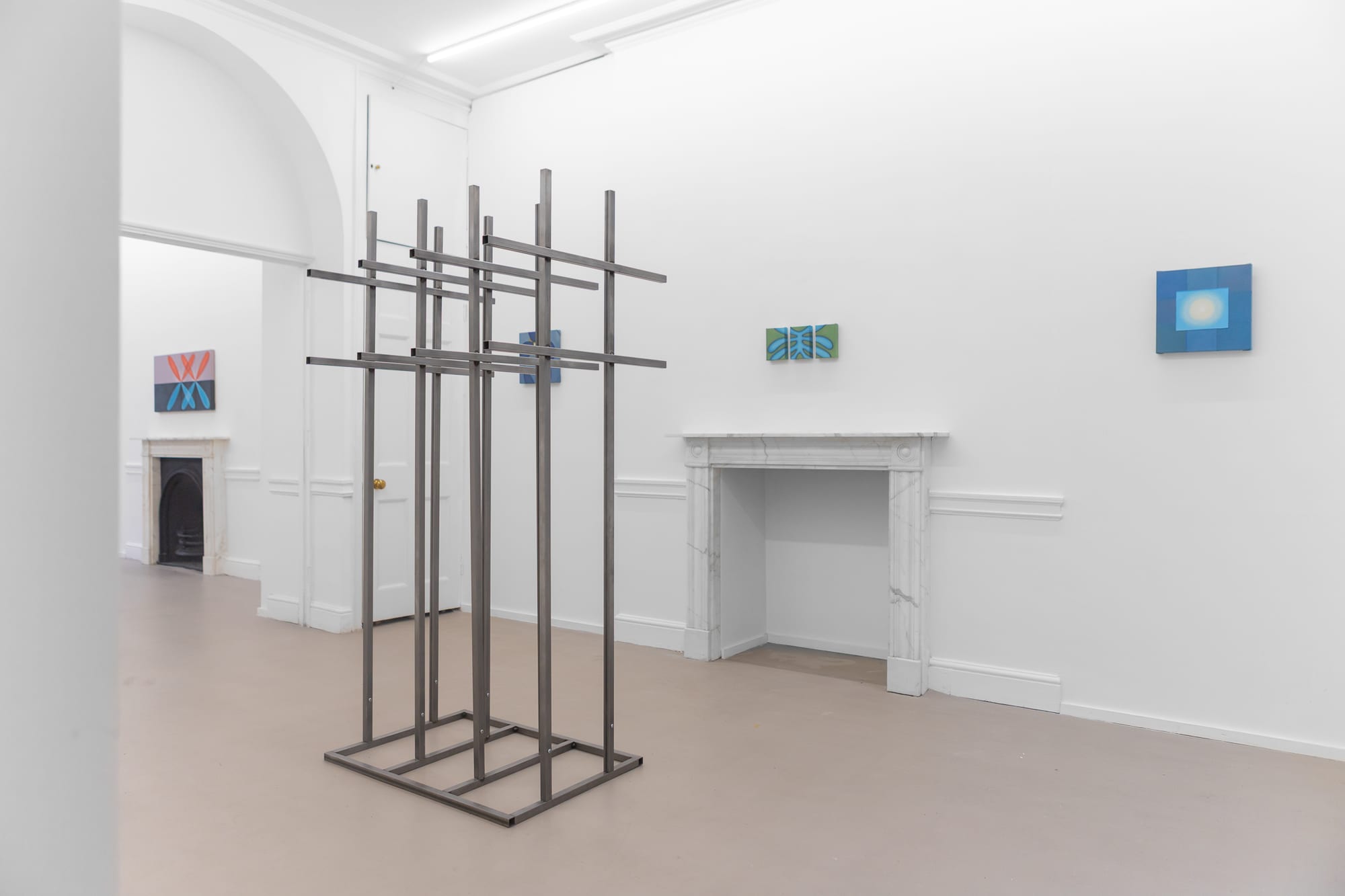 Installation view with a tall steel lattice sculpture and small paintings on the wall