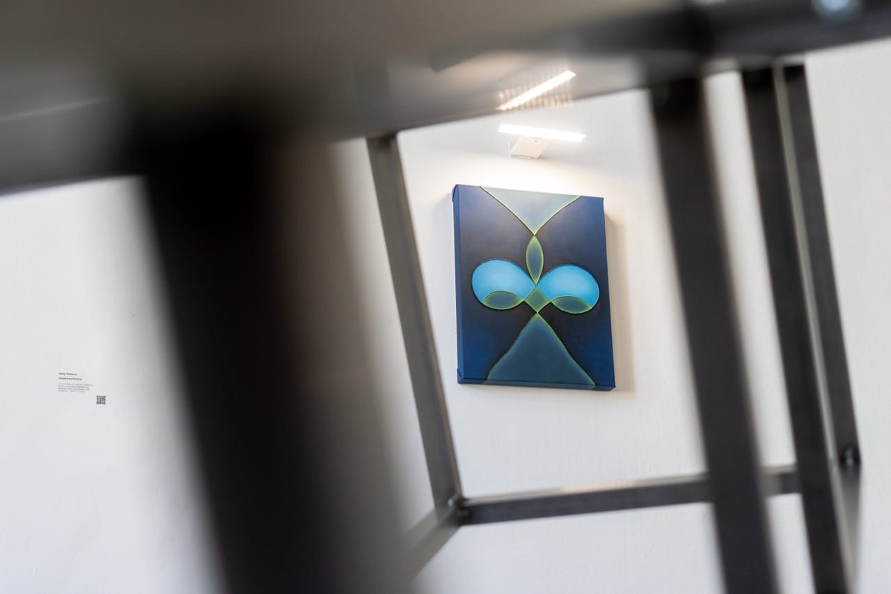 Steel frame sculpture viewed through its structure toward a blue painting