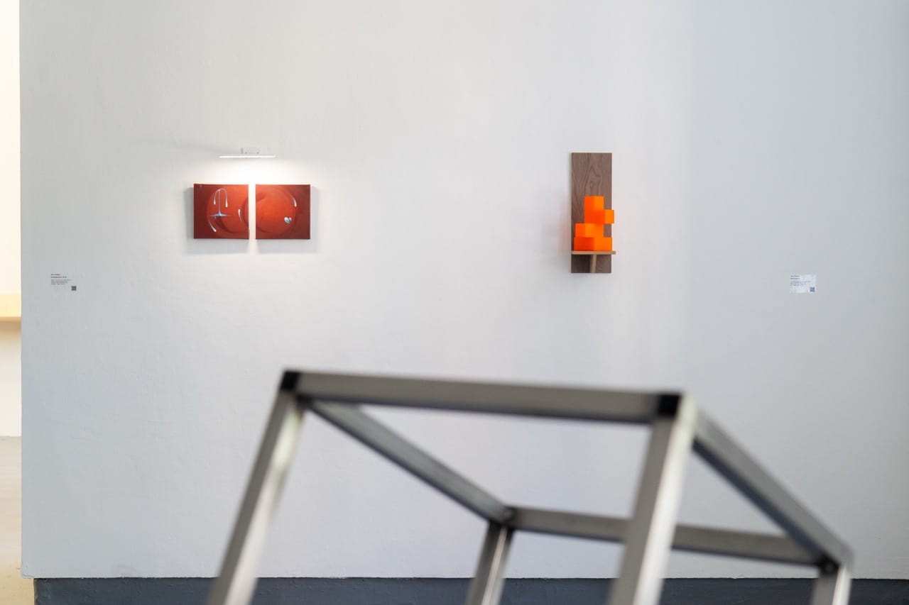 Gallery wall with red paintings and an orange sculptural form above a steel structure