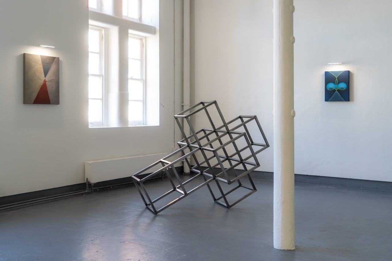 Crooked steel frame sculpture installed between paintings in a gallery