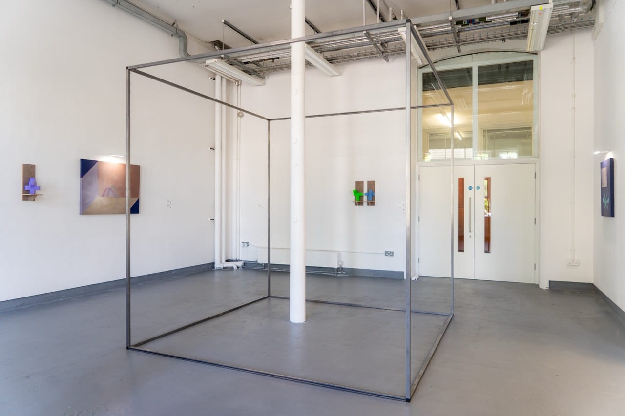 Wide view of the gallery with a large square steel frame and paintings