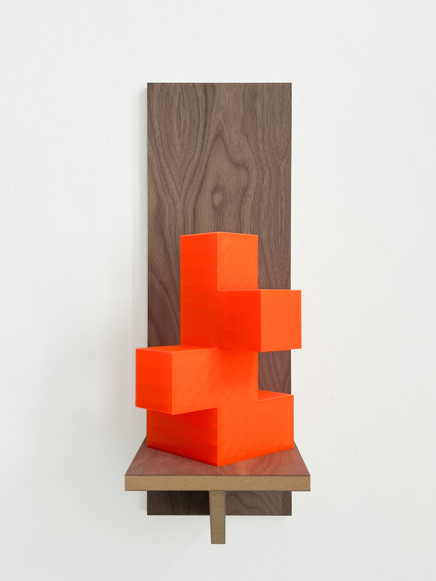 Neon-orange geometric wall sculpture mounted on a walnut panel