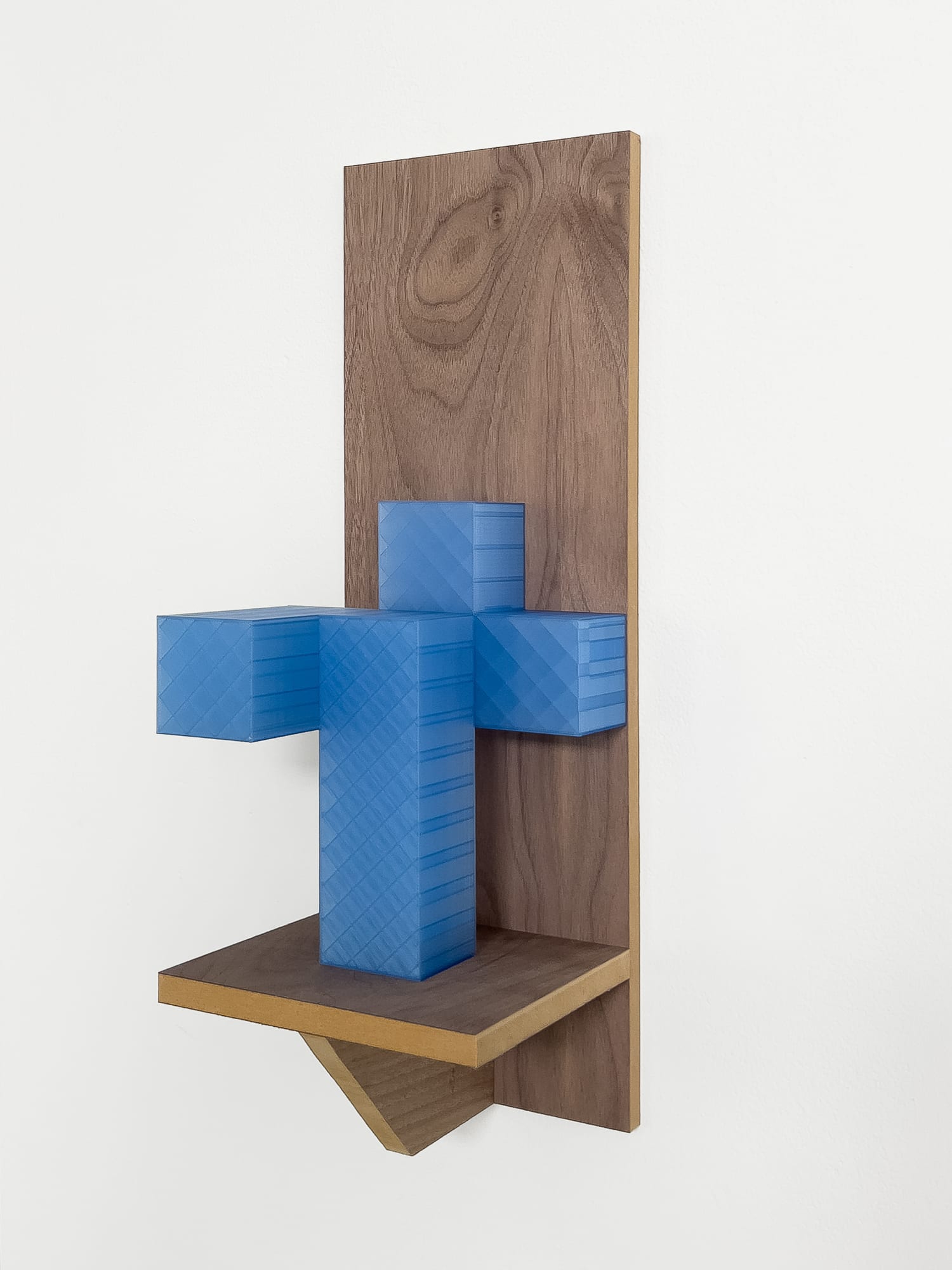 Blue geometric sculpture mounted on a wooden backing with brass-toned shelf details