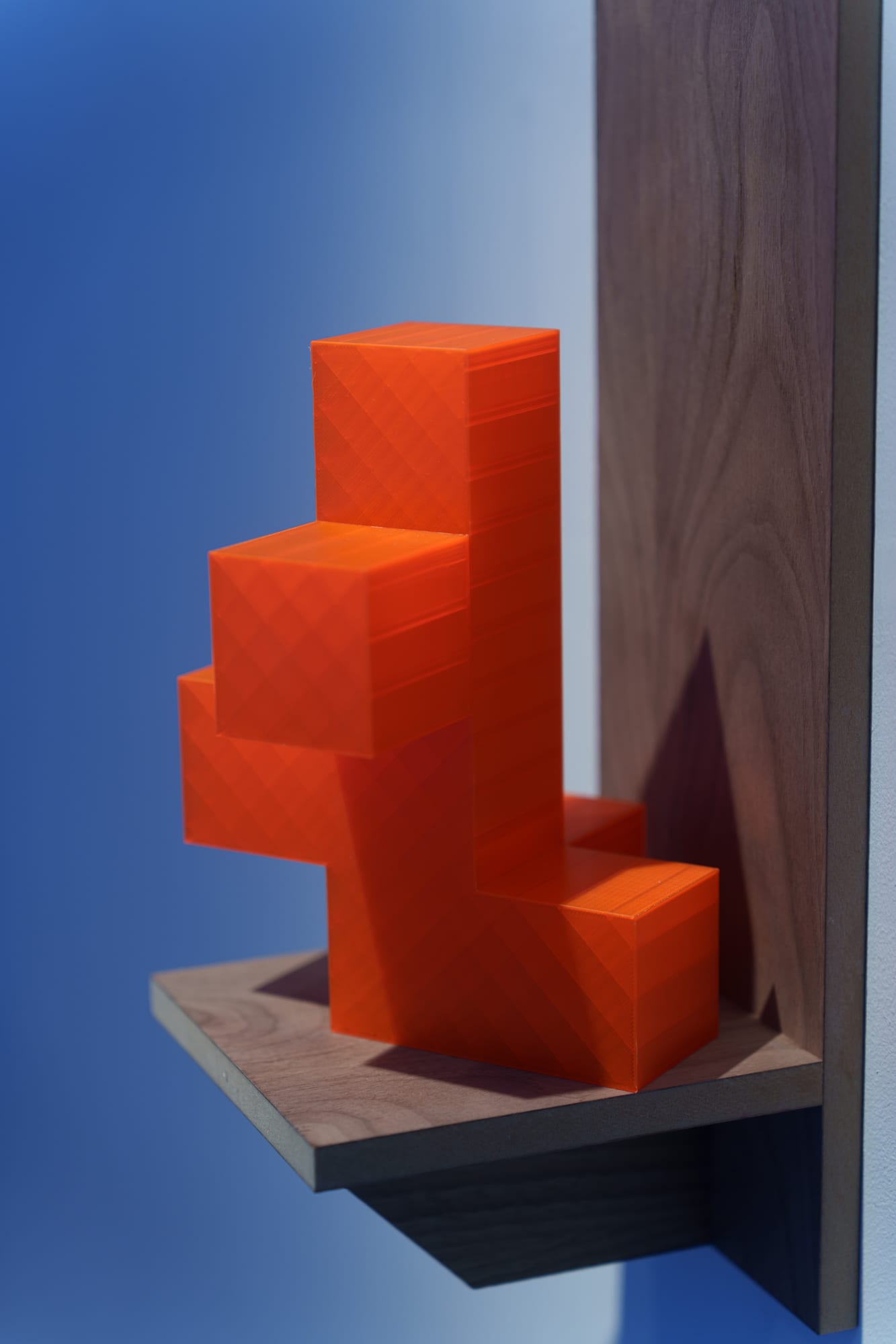 Colorful cross-shaped 3D printed sculptures mounted on wooden shelves beside paintings