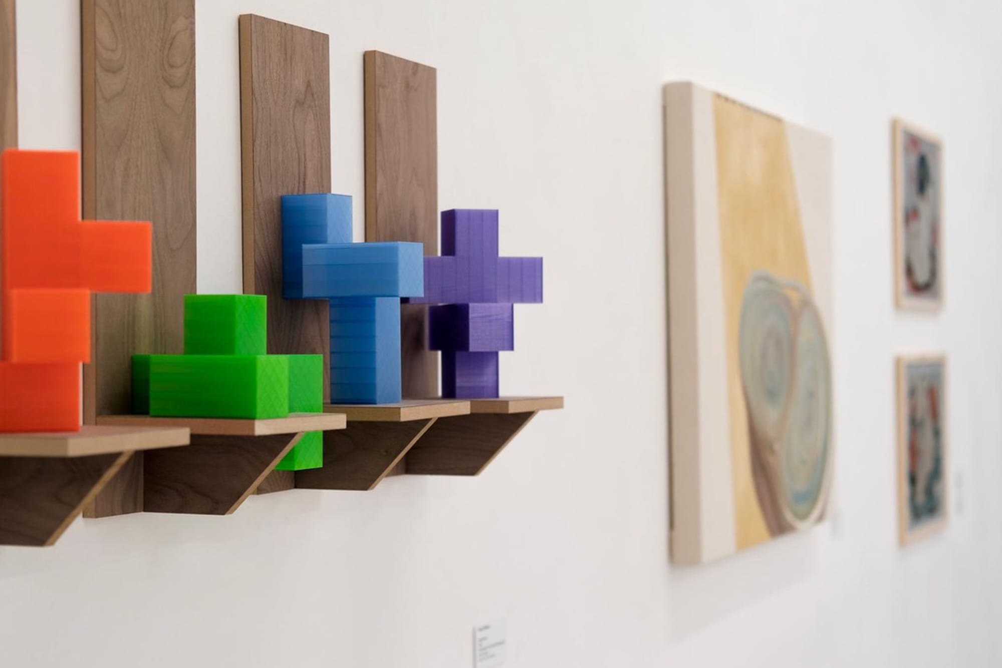 Detail view of orange, green, blue, and purple cross-shaped sculptures on wooden shelves